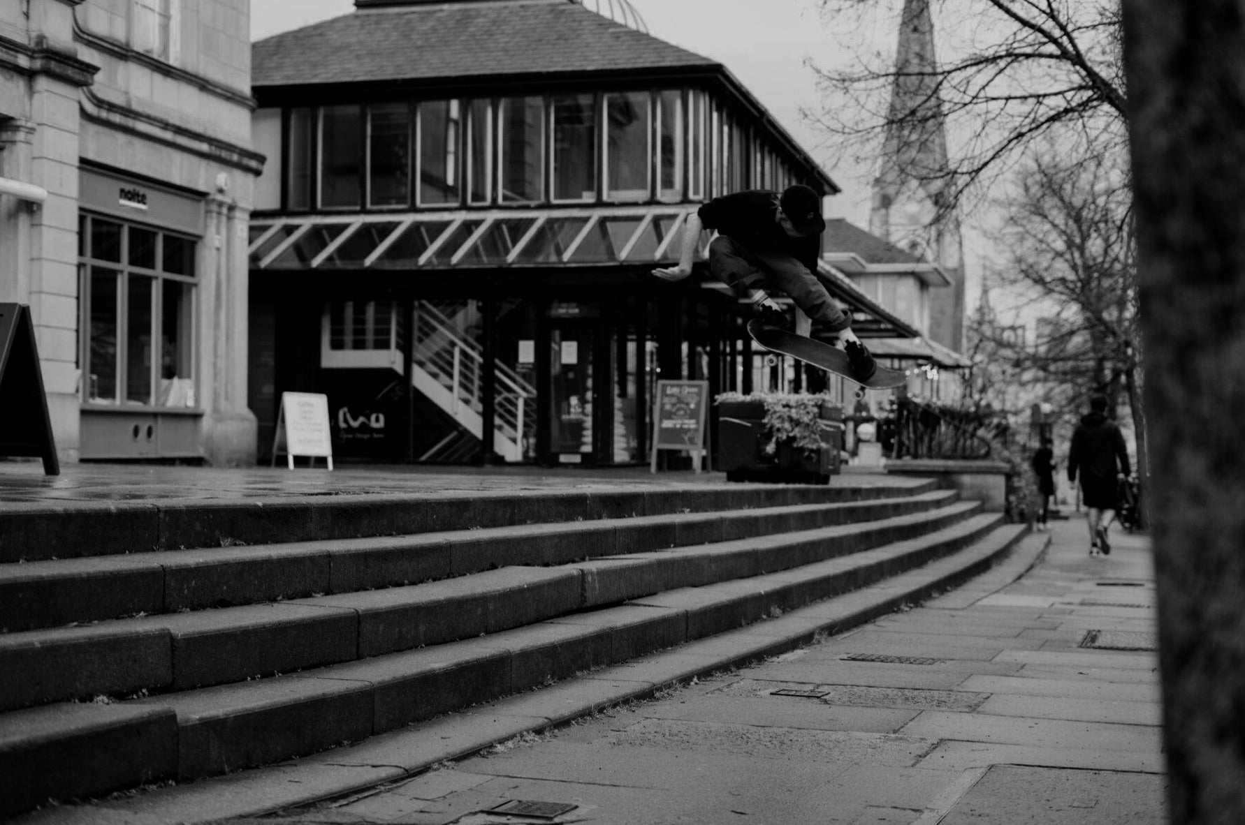 Black and white street image of a skater jumping over steps on a skateboard