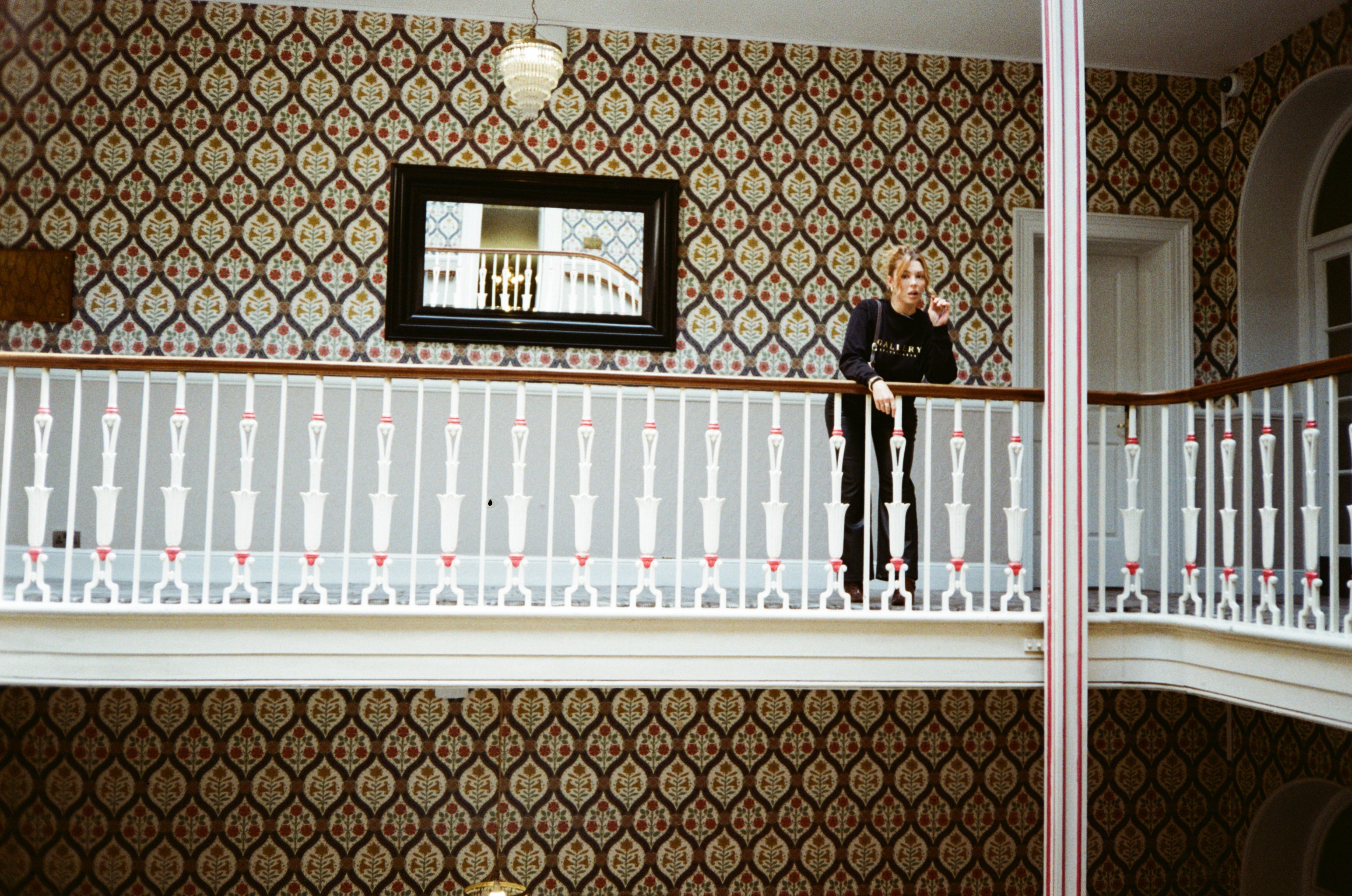 Model posing against a stylish bannister wearing the Monarch long-sleeved tee, vintage pattern wallpaper behind