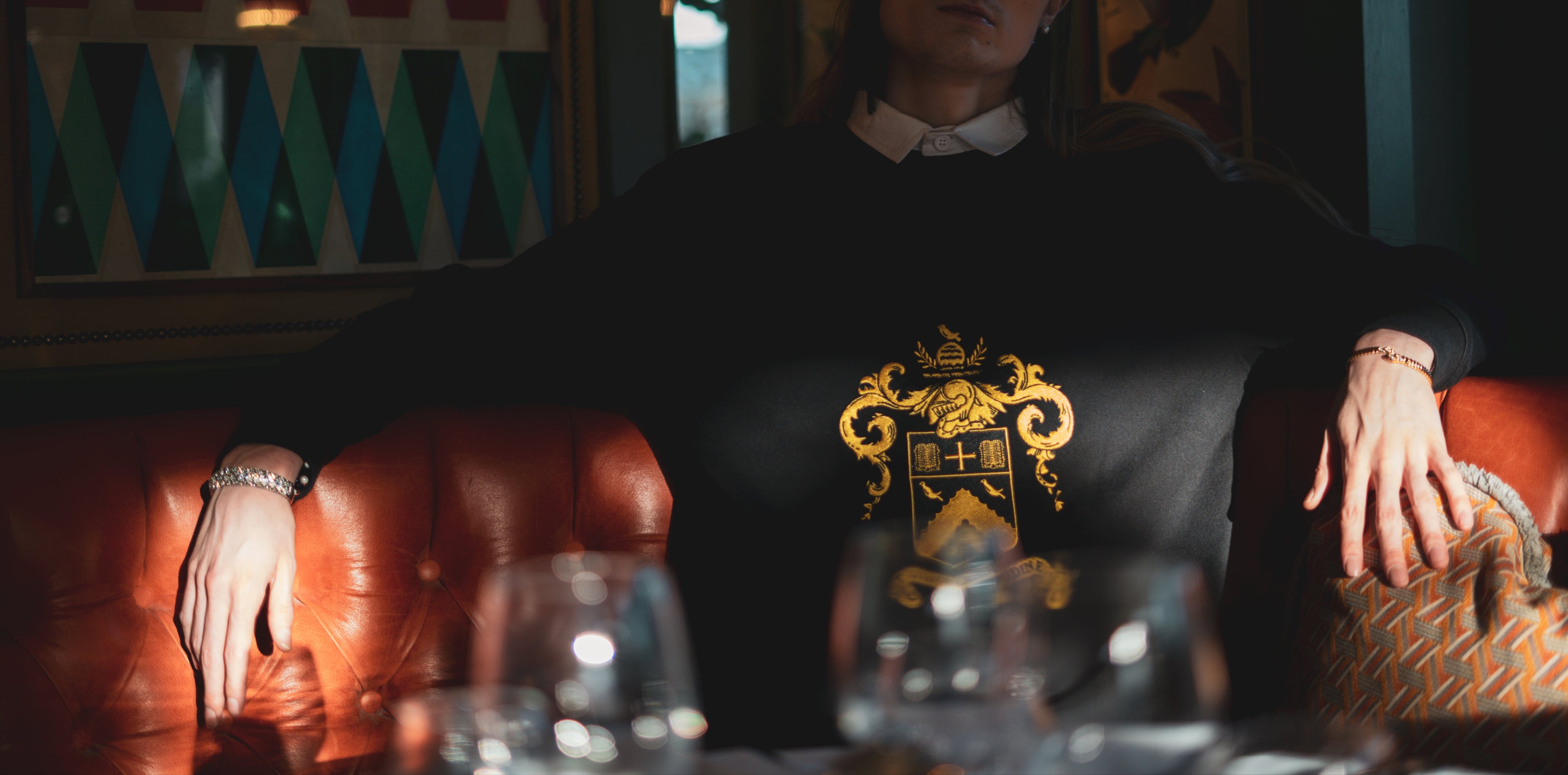 Model posing in a vintage leather booth, wearing the Heritage rugby shirt, the Herald trapper cap, artwork in the background