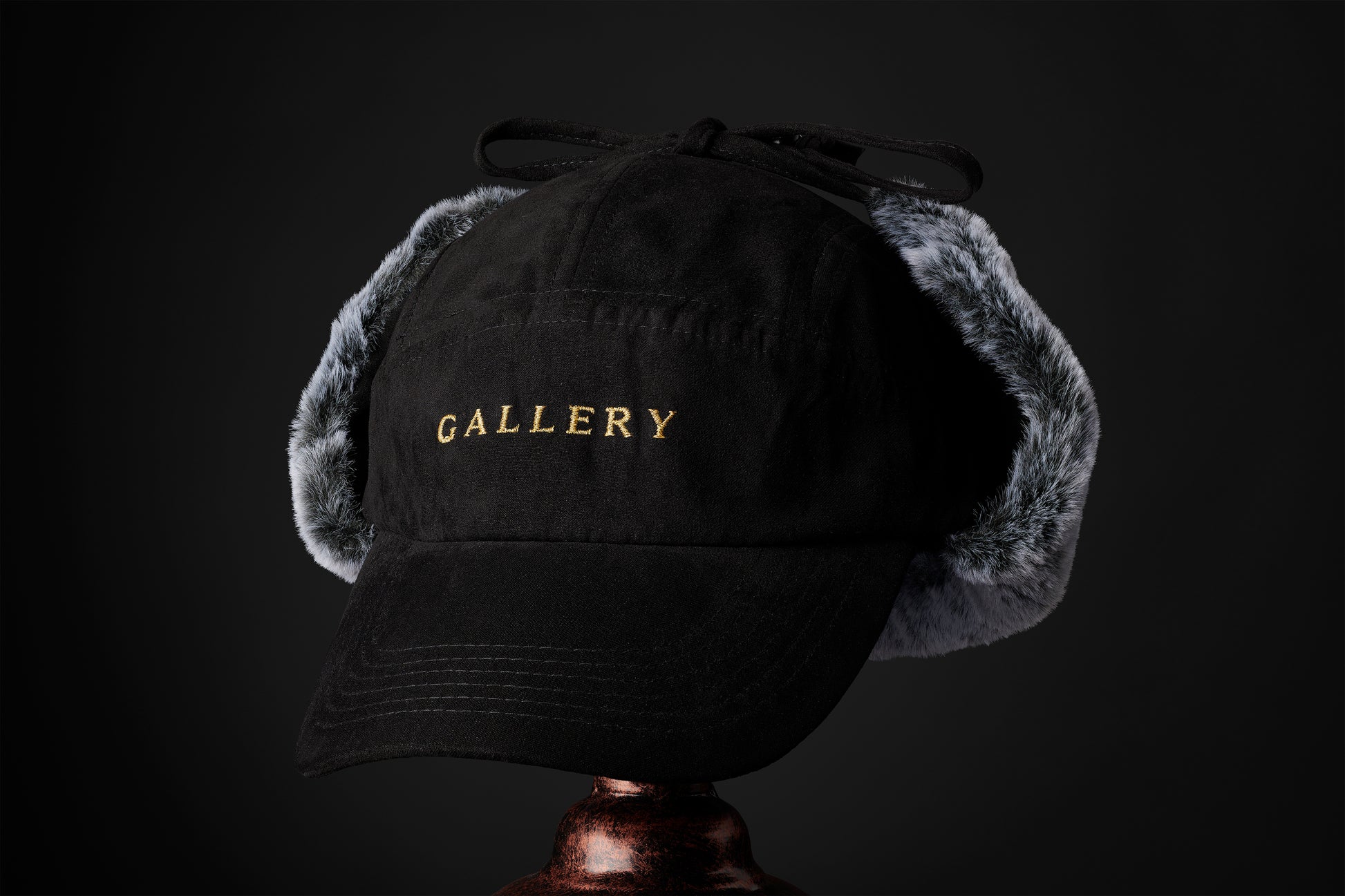 the Herald trapper cap, black with gold Gallery text logo and faux fur ear covers