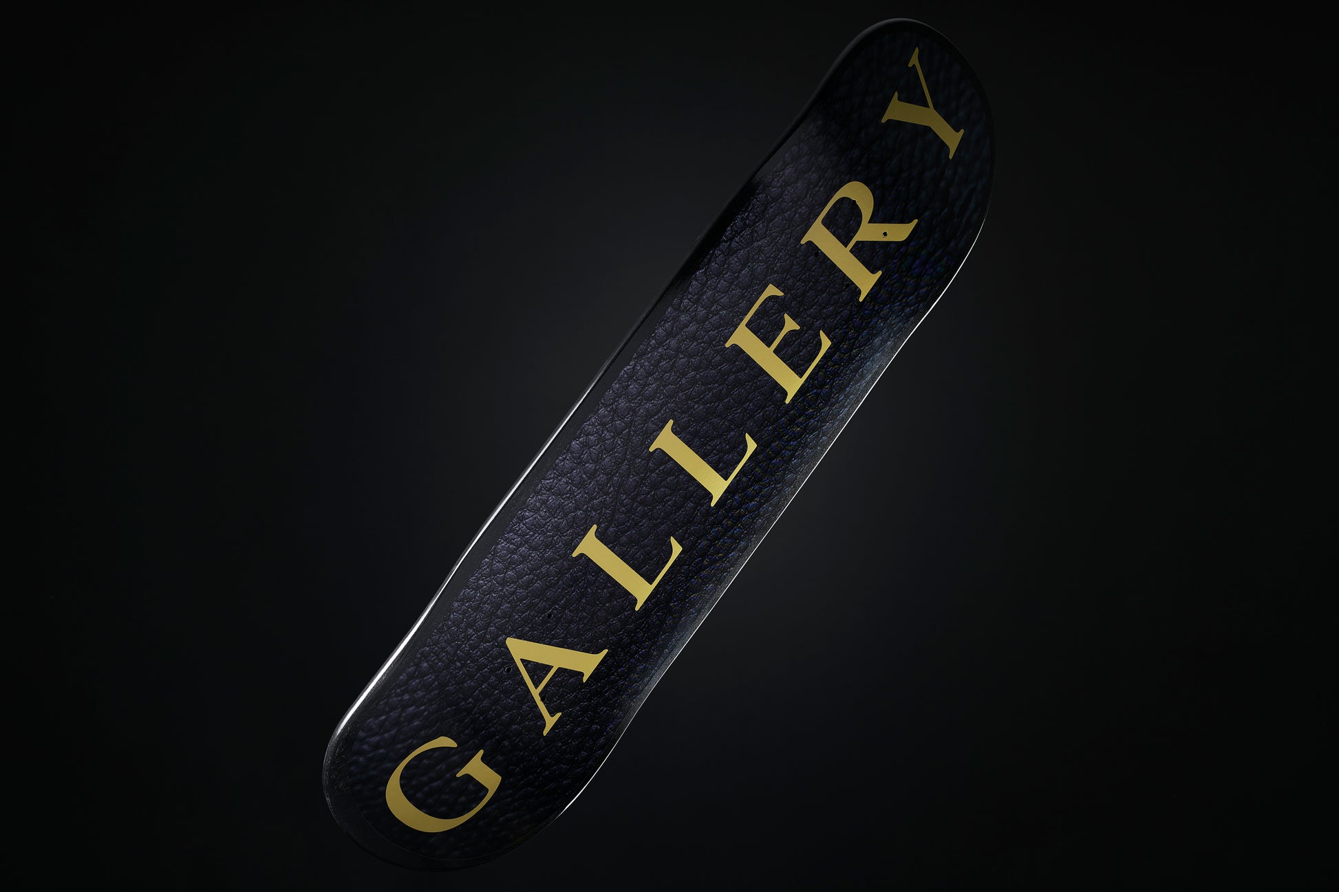 the Signature skateboard deck with black leather pattern design and large gold Gallery text logo